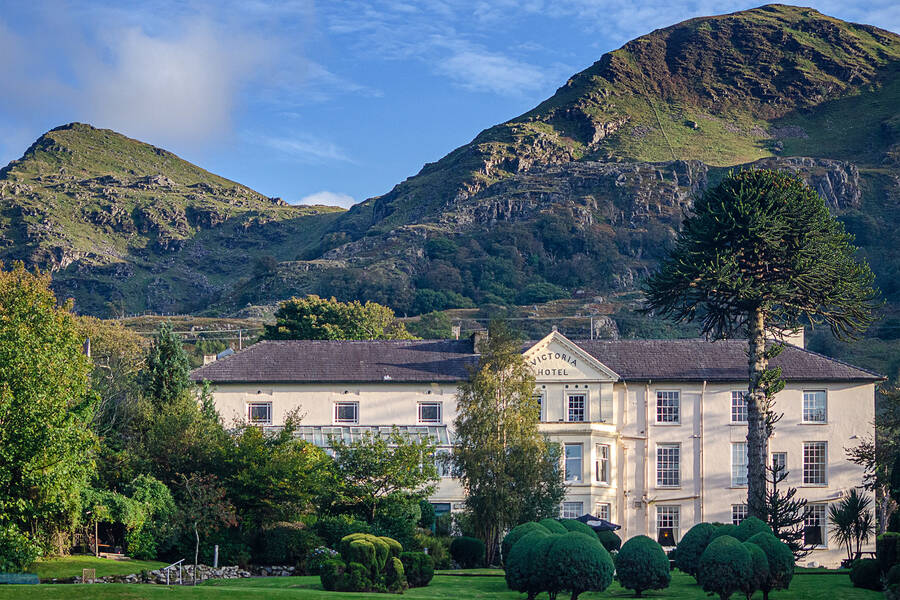 A view of the Royal Victoria Hotel in Snowdonia surrounded by lush gardens and mountains.