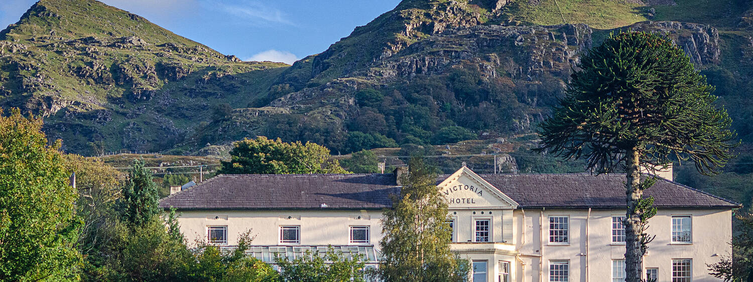 A view of the Royal Victoria Hotel in Snowdonia surrounded by lush gardens and mountains.